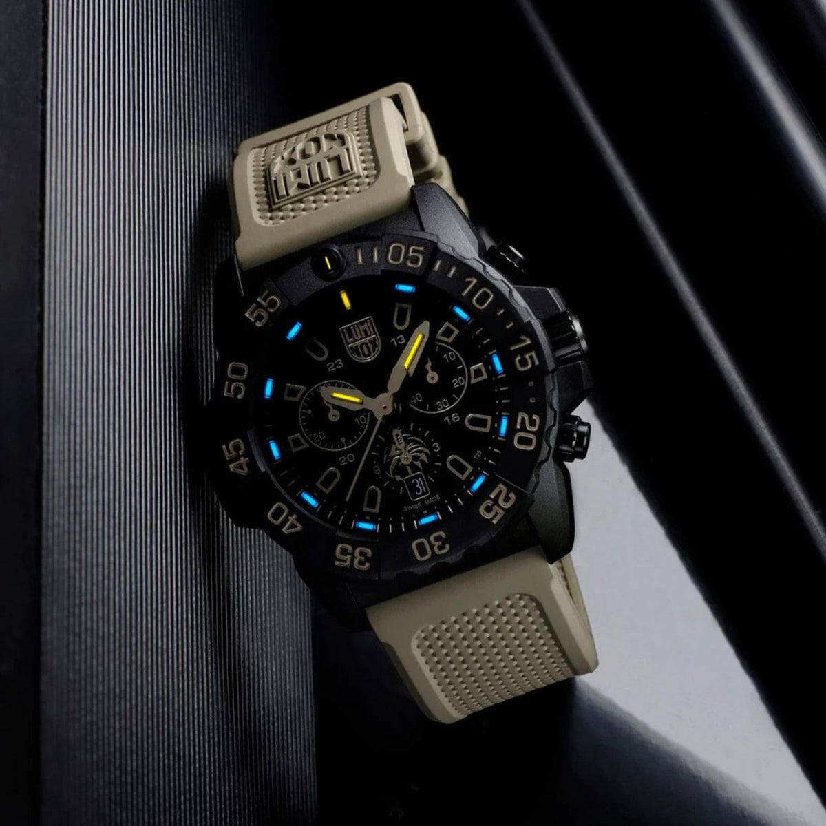 Black dial chronograph watch with tan rubber strap and blue illuminated hour markers