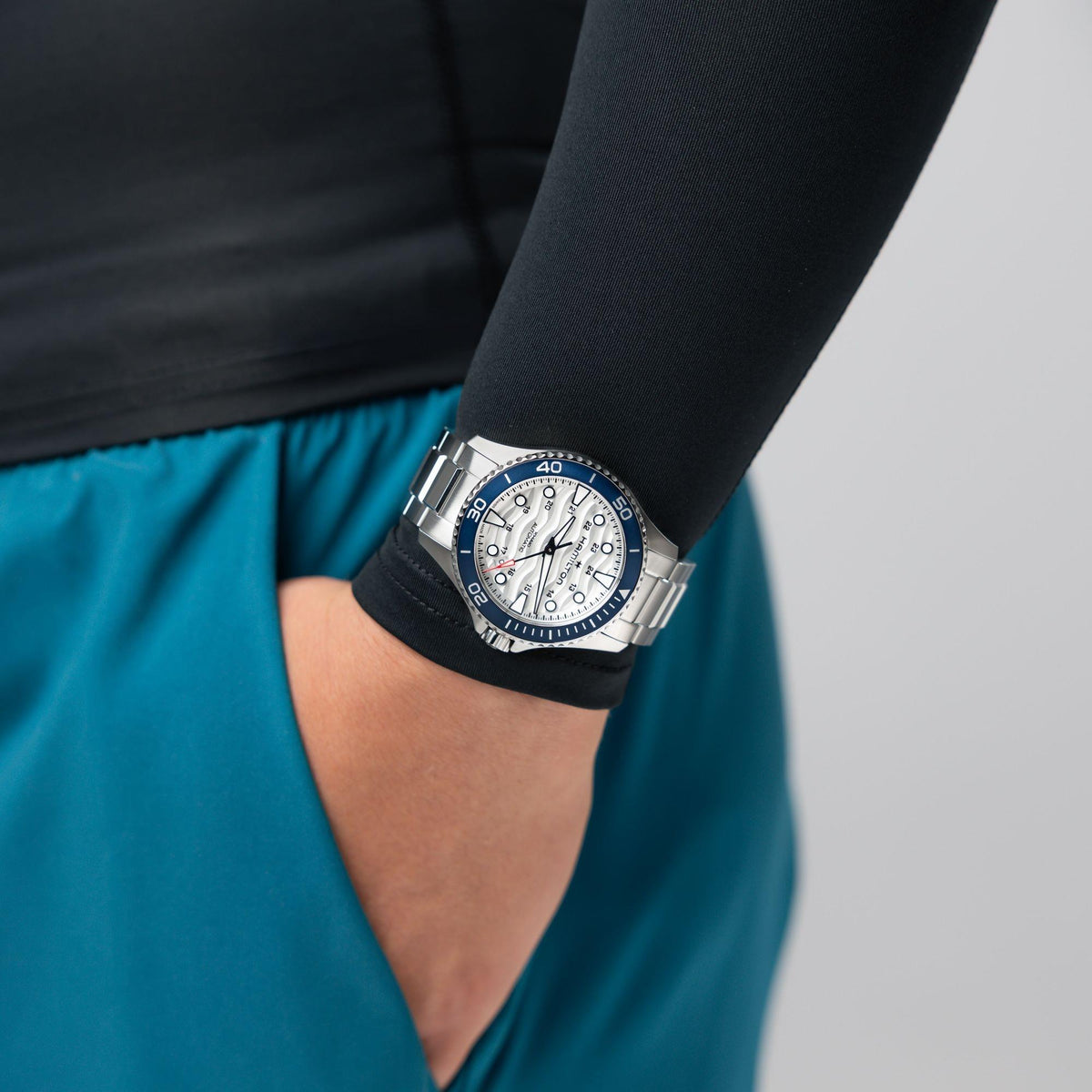 On-wrist view showing the Hamilton Khaki Navy Scuba H82425110 automatic watch worn over a black compression sleeve with teal shorts