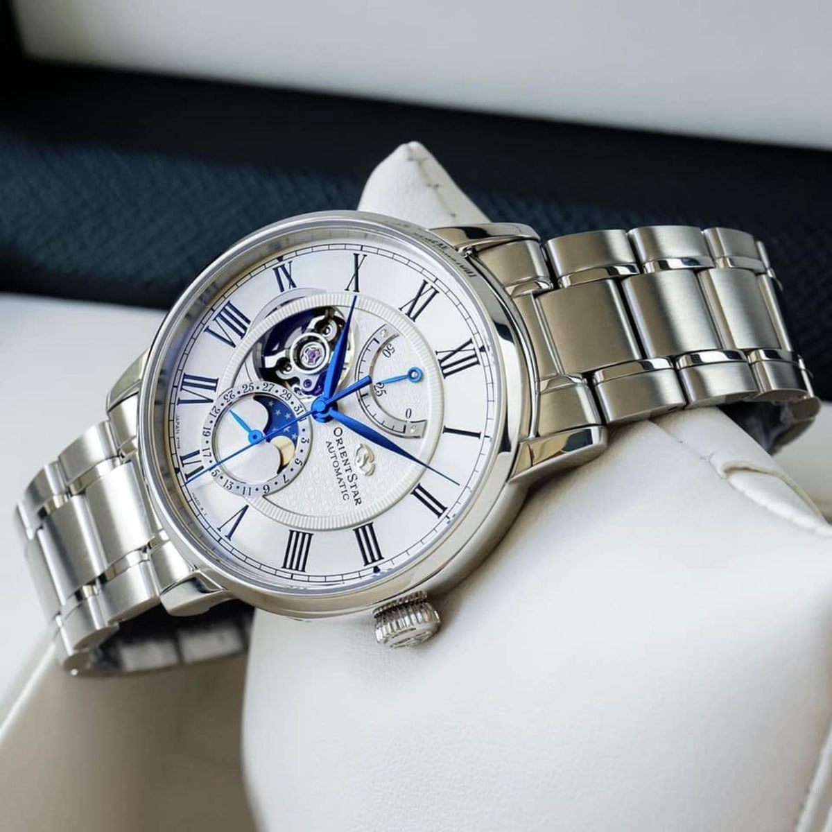 Semi-skeleton automatic watch with white dial, blue hands, and steel link bracelet