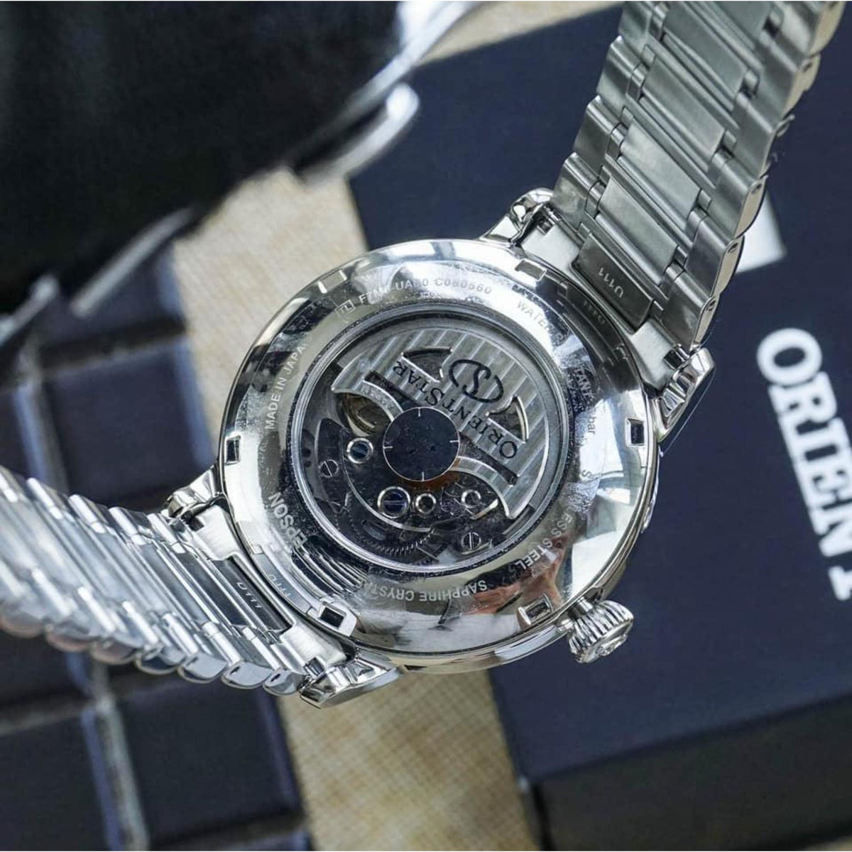 Steel watch back showing engraved movement through glass, on steel bracelet