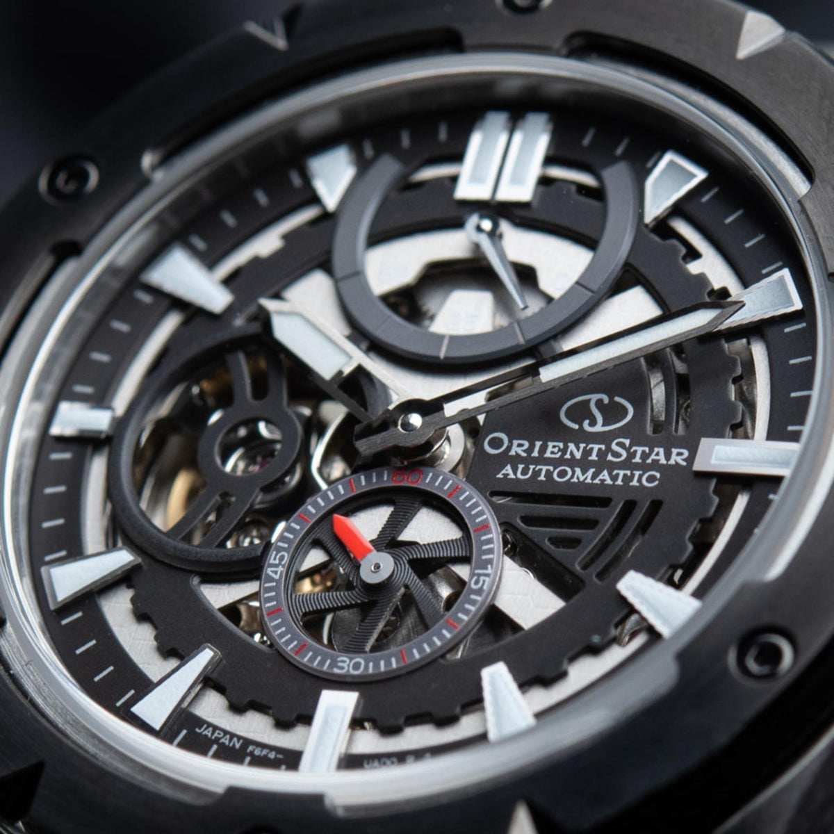 Men's automatic skeleton watch dial close-up, exposed balance wheel and red accent.