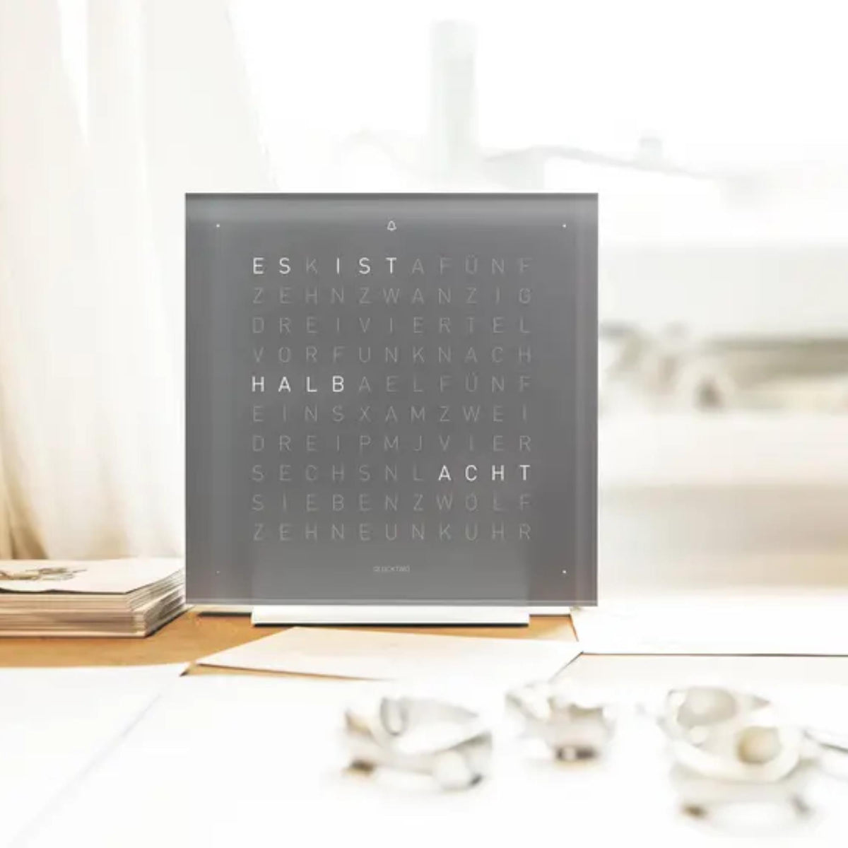 Table clock with square grey panel and illuminated English word display, standing on base