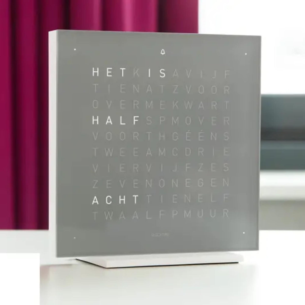 Table clock with square grey face showing illuminated English words on its front