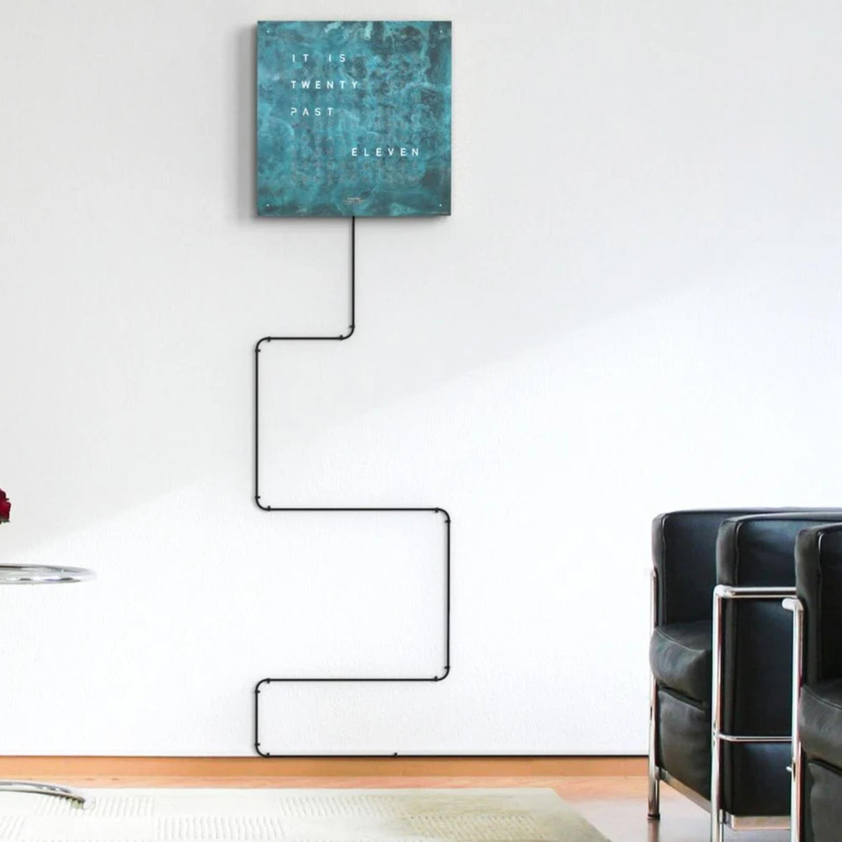 Square wall clock with teal face and black cable connection to the rear