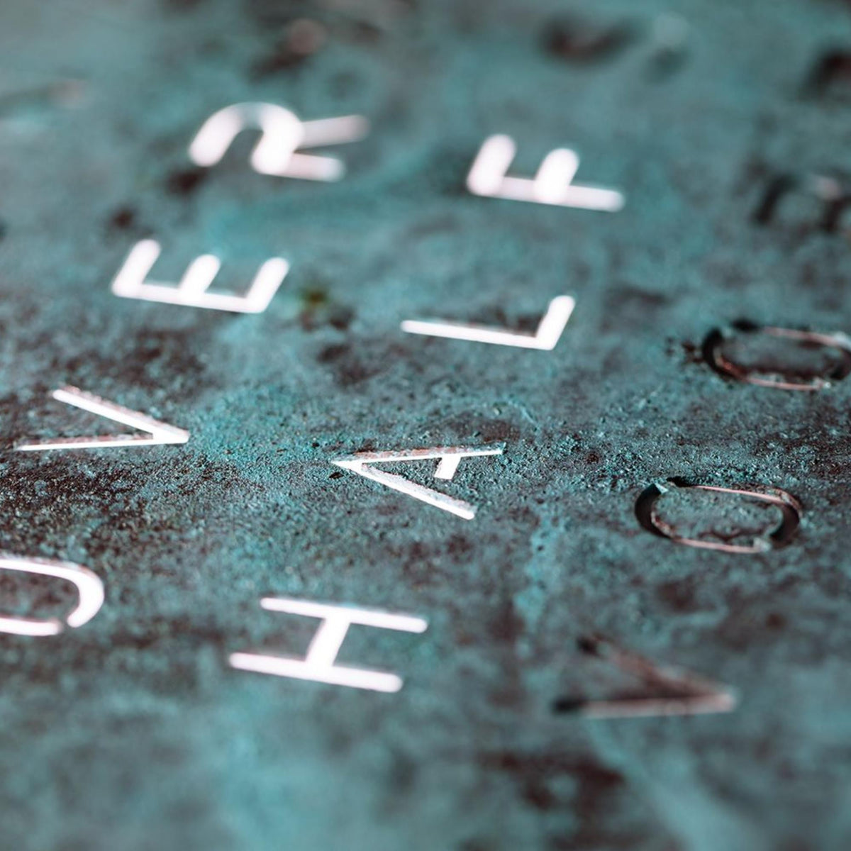 Close-up of teal clock dial with raised white letter tiles and textured finish