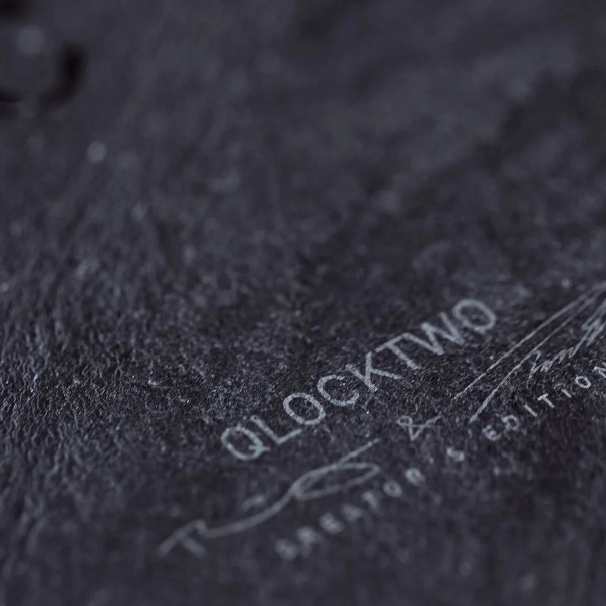 QLOCKTWO wall clock face close-up with 'QLOCKTWO' embossed on dark textured surface