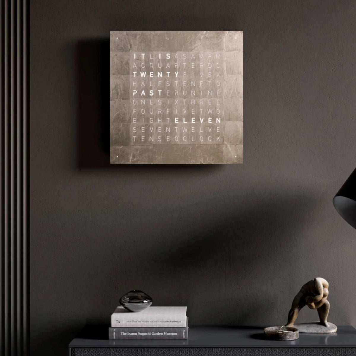 QLOCKTWO gold word clock mounted on the wall above a shelf with decor