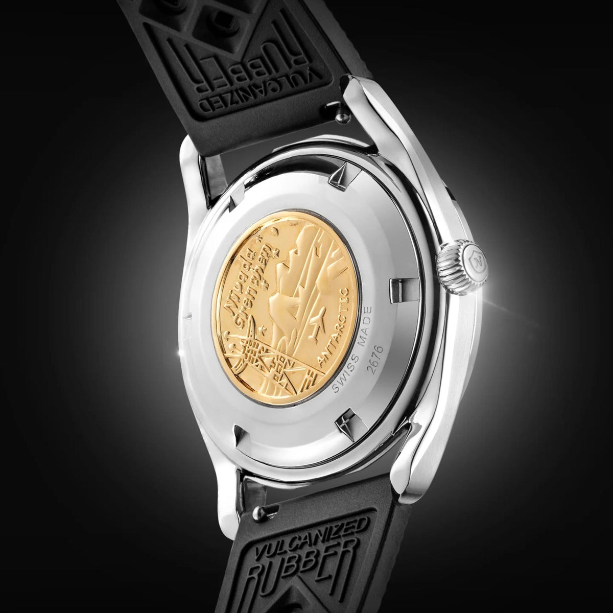 Men's watch caseback with gold medallion insert and engraved markings, black rubber strap