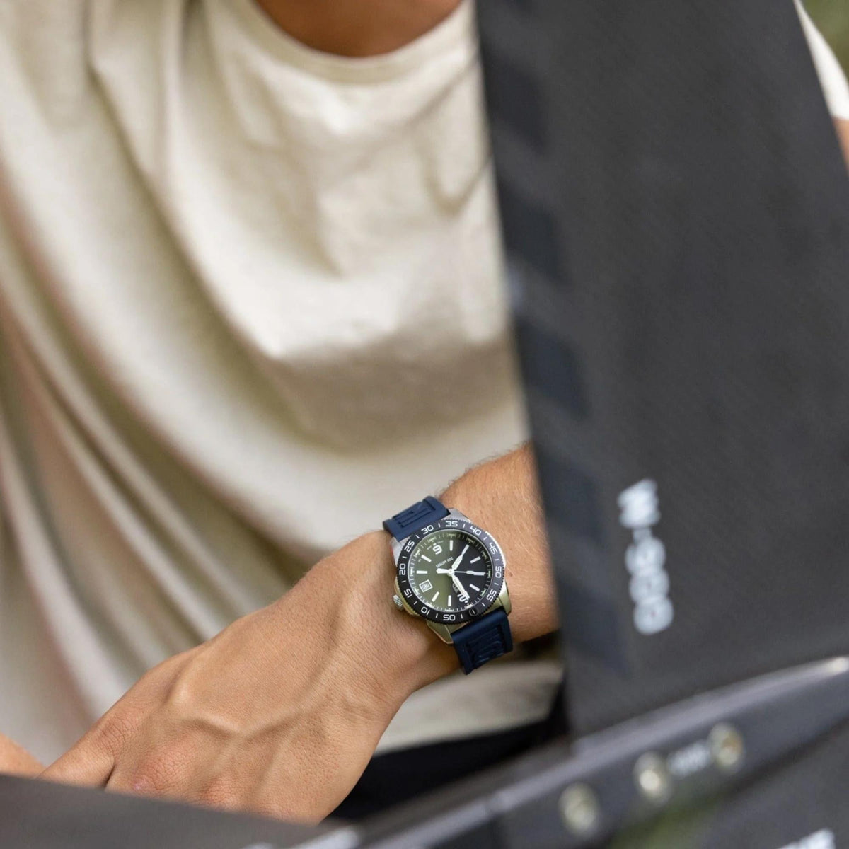 Wrist-worn diver watch with dark dial and blue strap, luminous markers visible