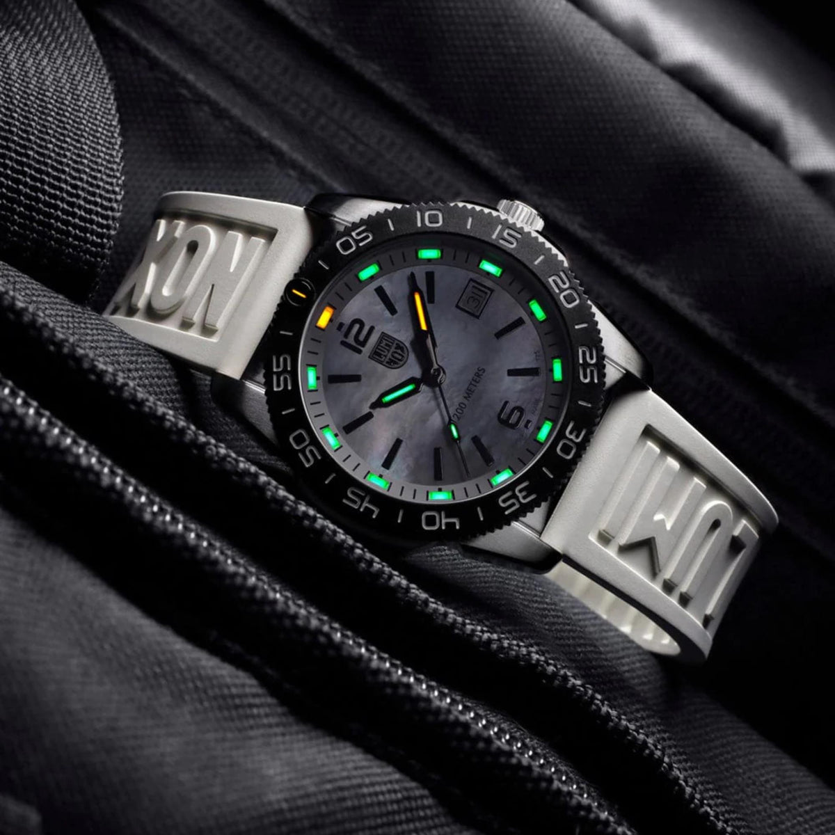 Close-up diver watch with white textured dial, luminous green and orange accents