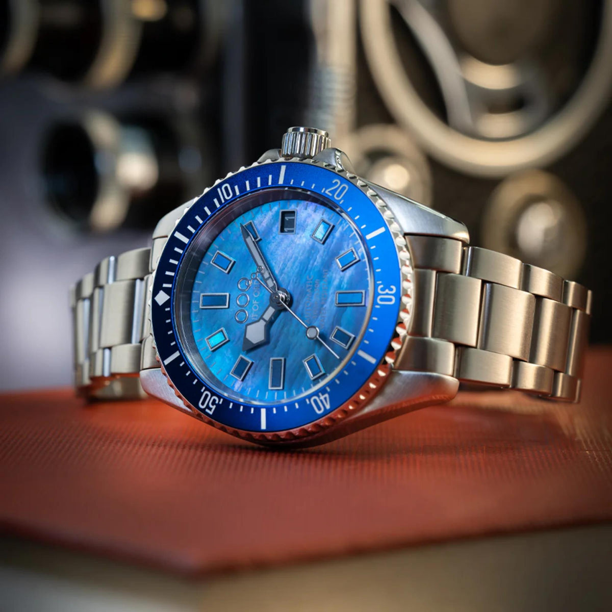 Men's automatic watch with blue dial and metal bracelet resting on a table