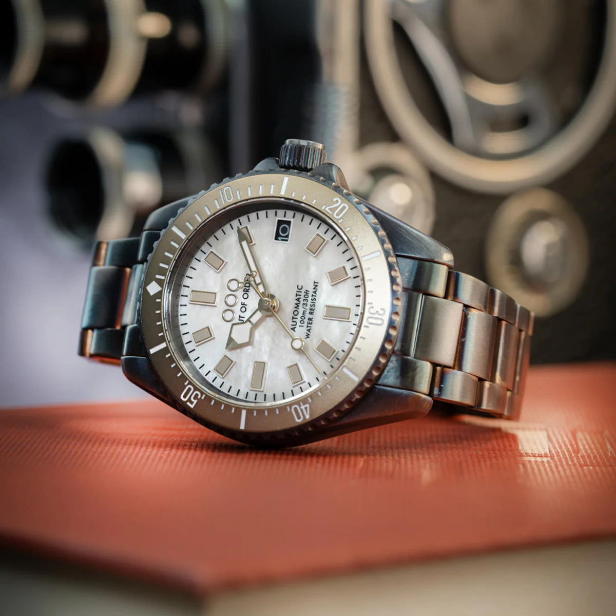 Men's automatic wristwatch with ivory dial and steel bracelet resting on a surface