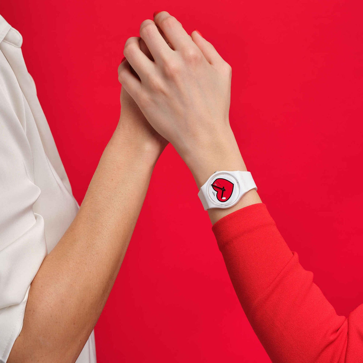 Clasping hands against a red background, showcasing the white Swatch Originals Love O'Clock watch (GW718) paired with a vibrant red sleeve