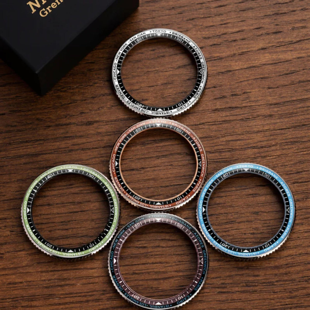 Five interchangeable watch bezels for the Nivada Grenchen Chronoking are arranged on a wooden surface