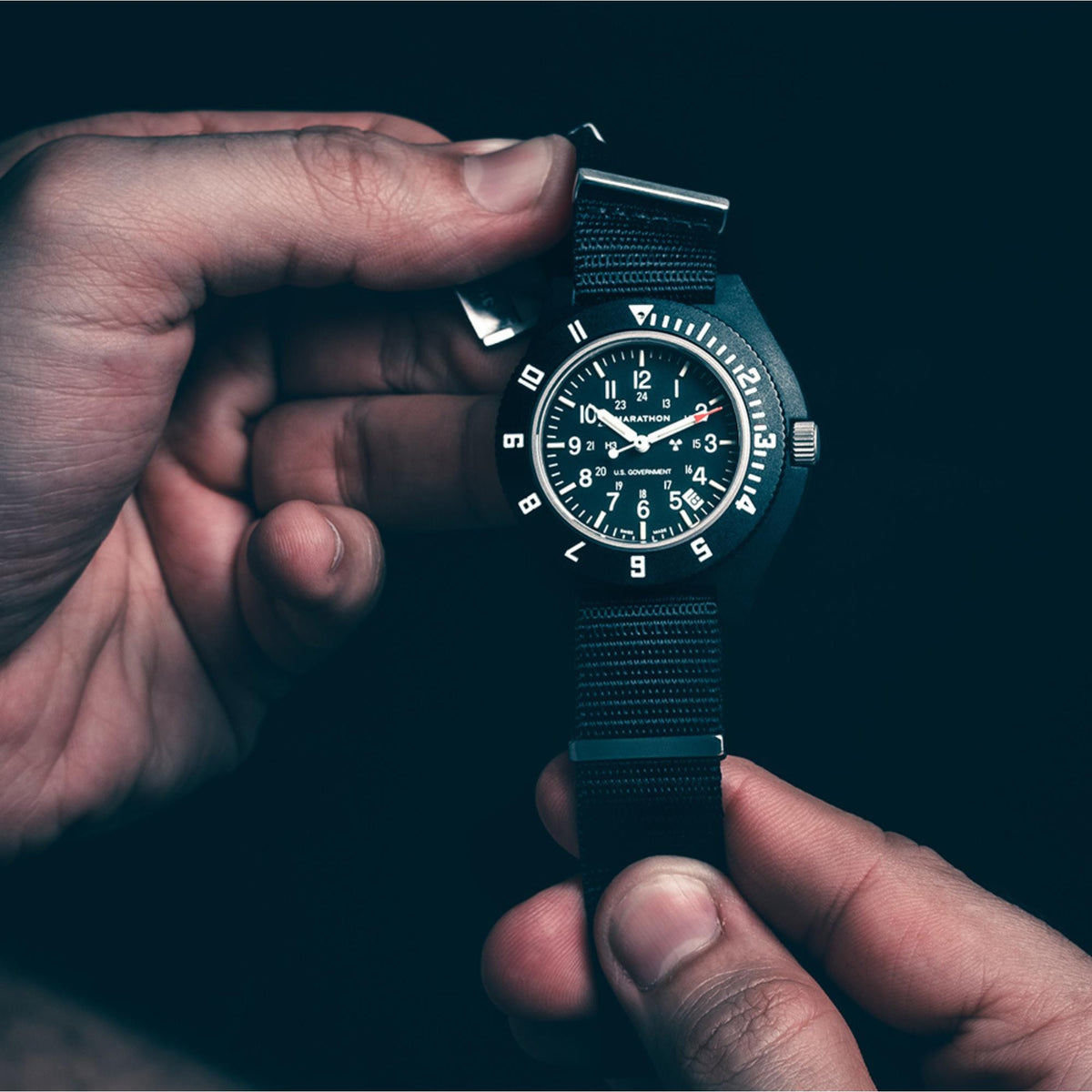 Marathon Navigator WW194013BK-0001 men's quartz timepiece held in hands against dark background