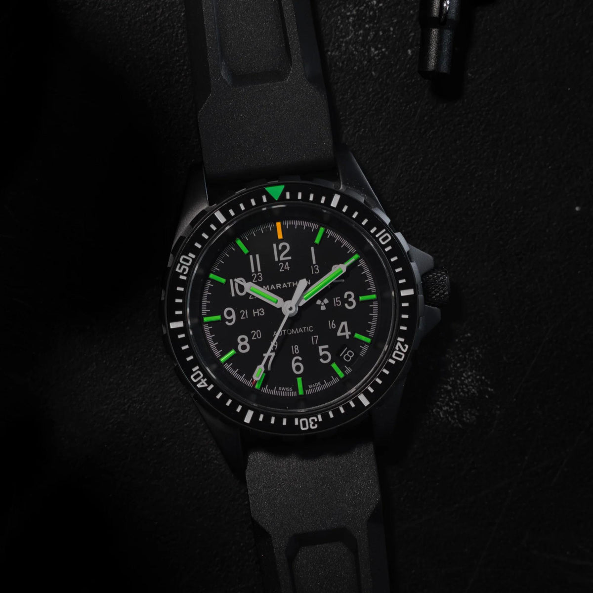 Marathon MSAR Anthracite watch showing glowing illuminated markers and hands on black dial in dark setting