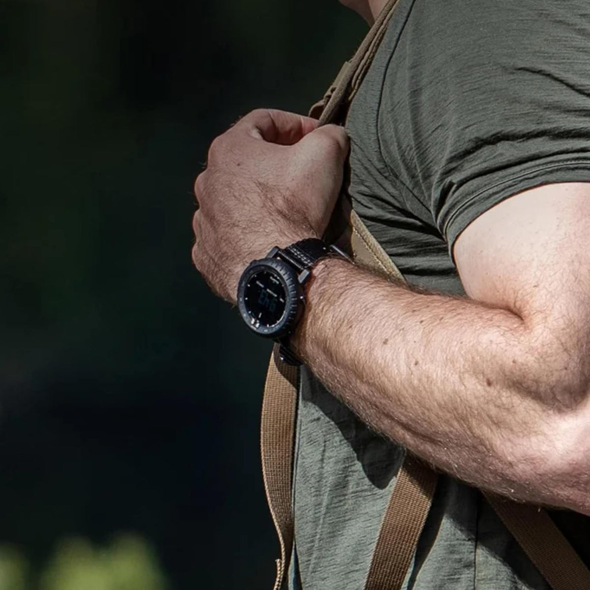 Suunto Core SS014279010 wrist action shot showing a hiker wearing an outdoor digital watch with a green t-shirt and a backpack strap