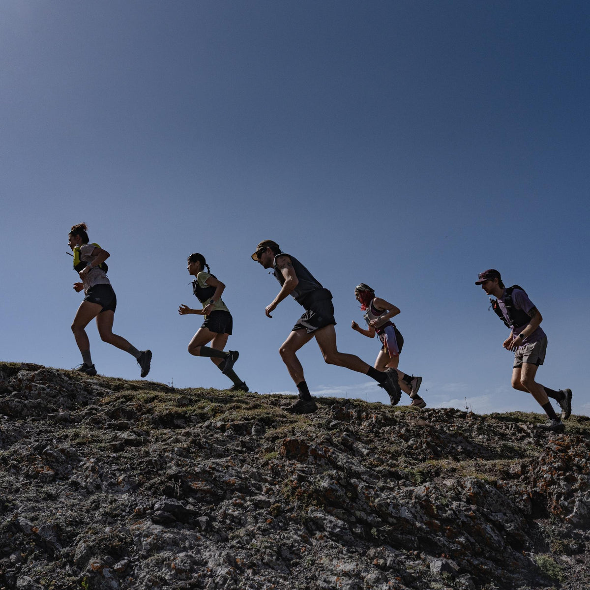 Suunto Race 3S SS051647000 lifestyle view showing a group of trail runners ascending a mountain ridge under a clear sky