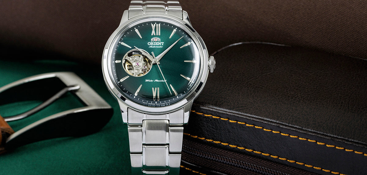Men's steel automatic watch on wrist with green dial, Roman numerals, open-heart movement