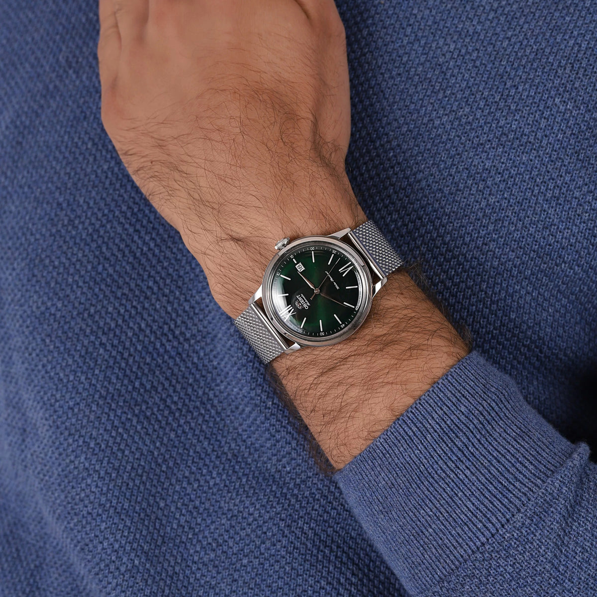 Automatic watch with green dial and steel mesh bracelet worn on a man’s wrist