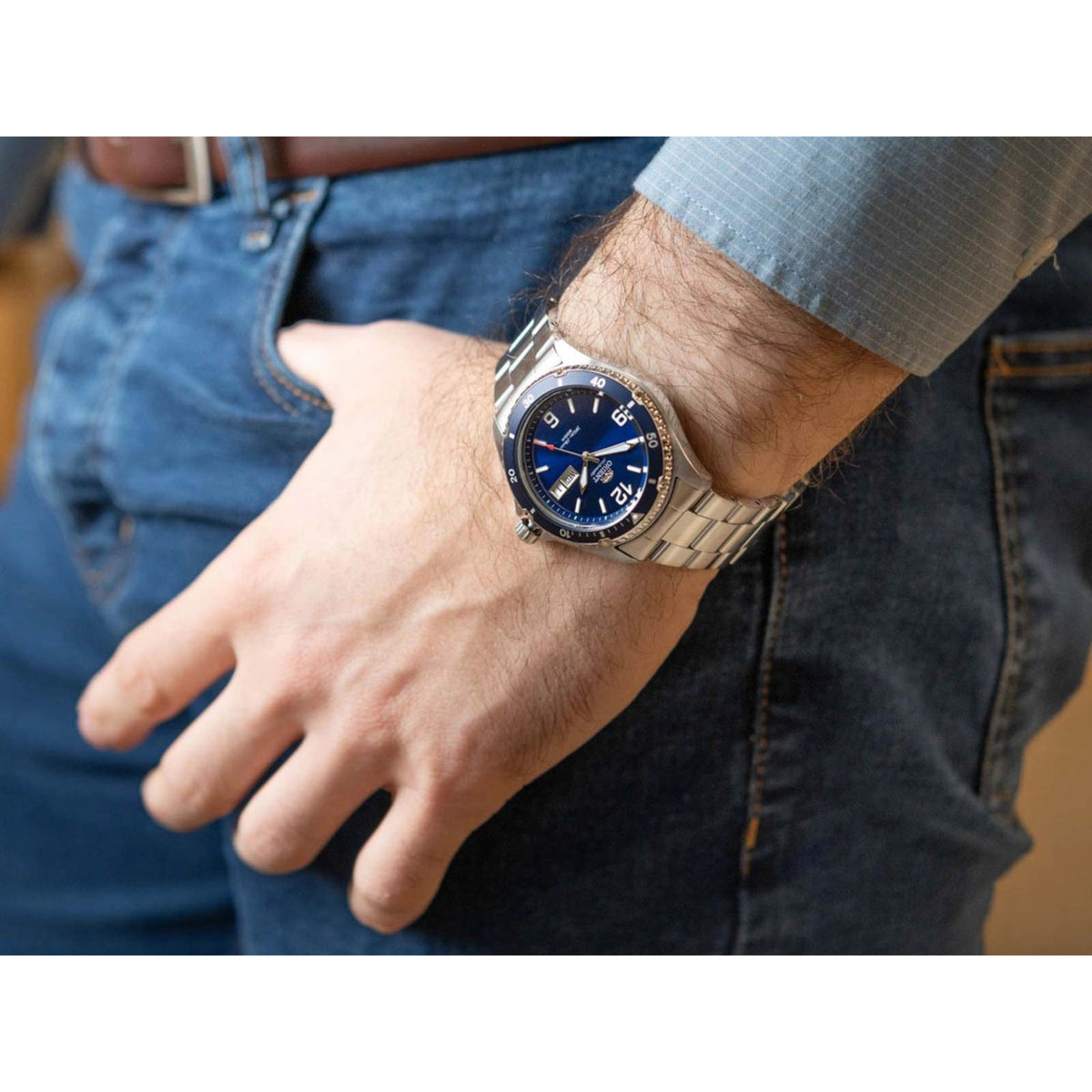 Men's steel automatic watch with blue dial worn on wrist, showing day/date window