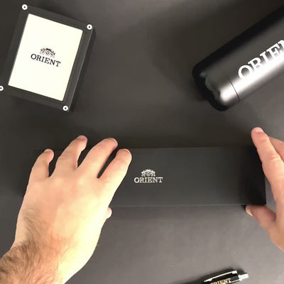 Hands opening the official presentation box for the Orient Bambino RA-AK0701S30B mechanical wrist watch