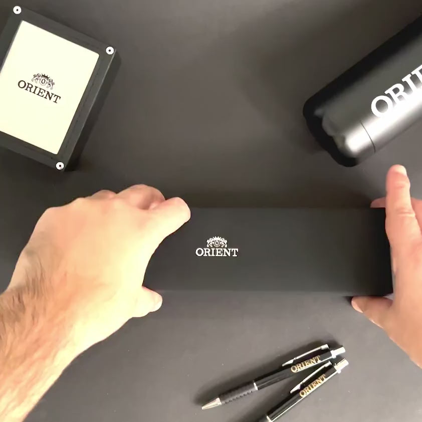 Orient Bambino TAC00009W0 watch packaging set being unboxed on a dark desk surface