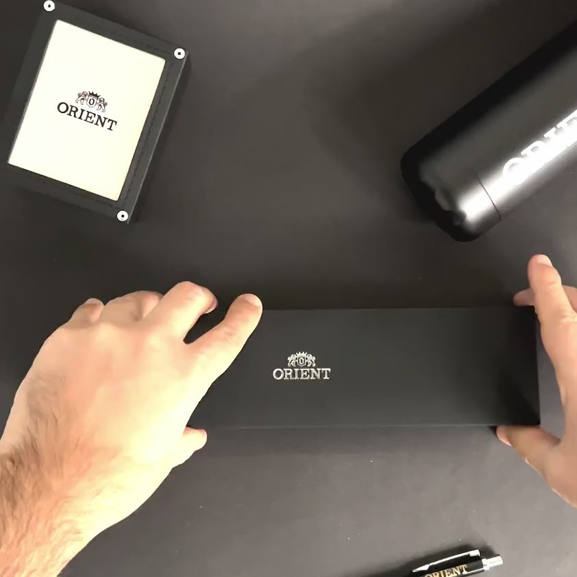 Hands opening official Orient Bambino RA-AC0P01E30B black presentation box on dark surface