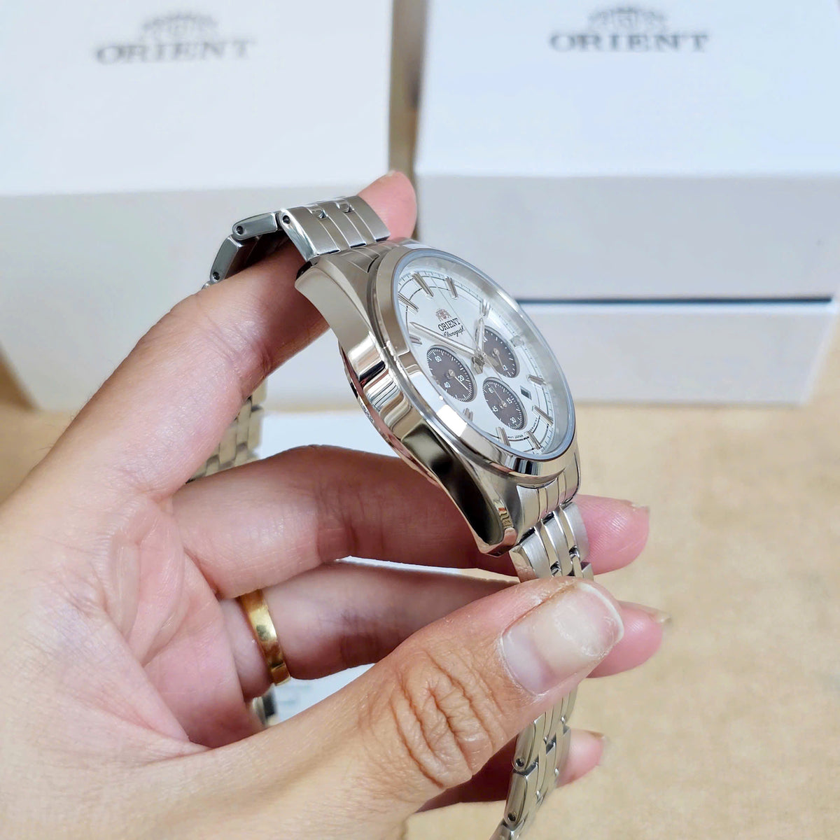 Men’s solar chronograph watch held near the wrist, steel bracelet and crown visible