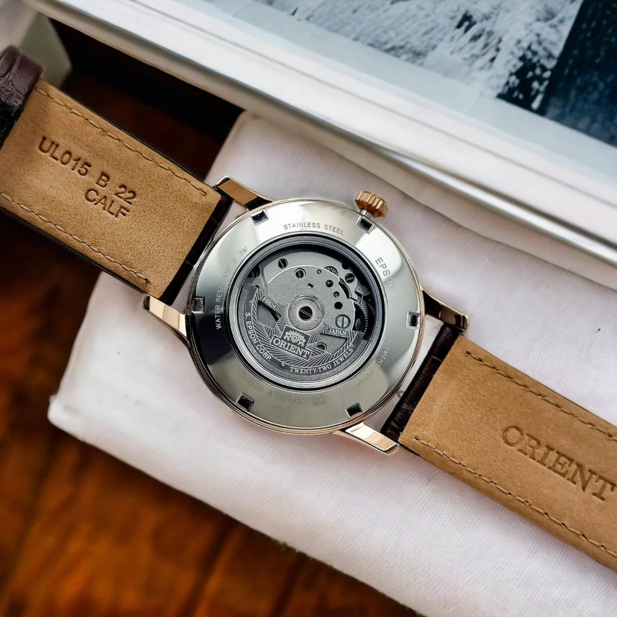 Orient Bambino RA-AK0009T30B wristwatch showing its exhibition caseback on white cloth with a brown leather strap and metal back