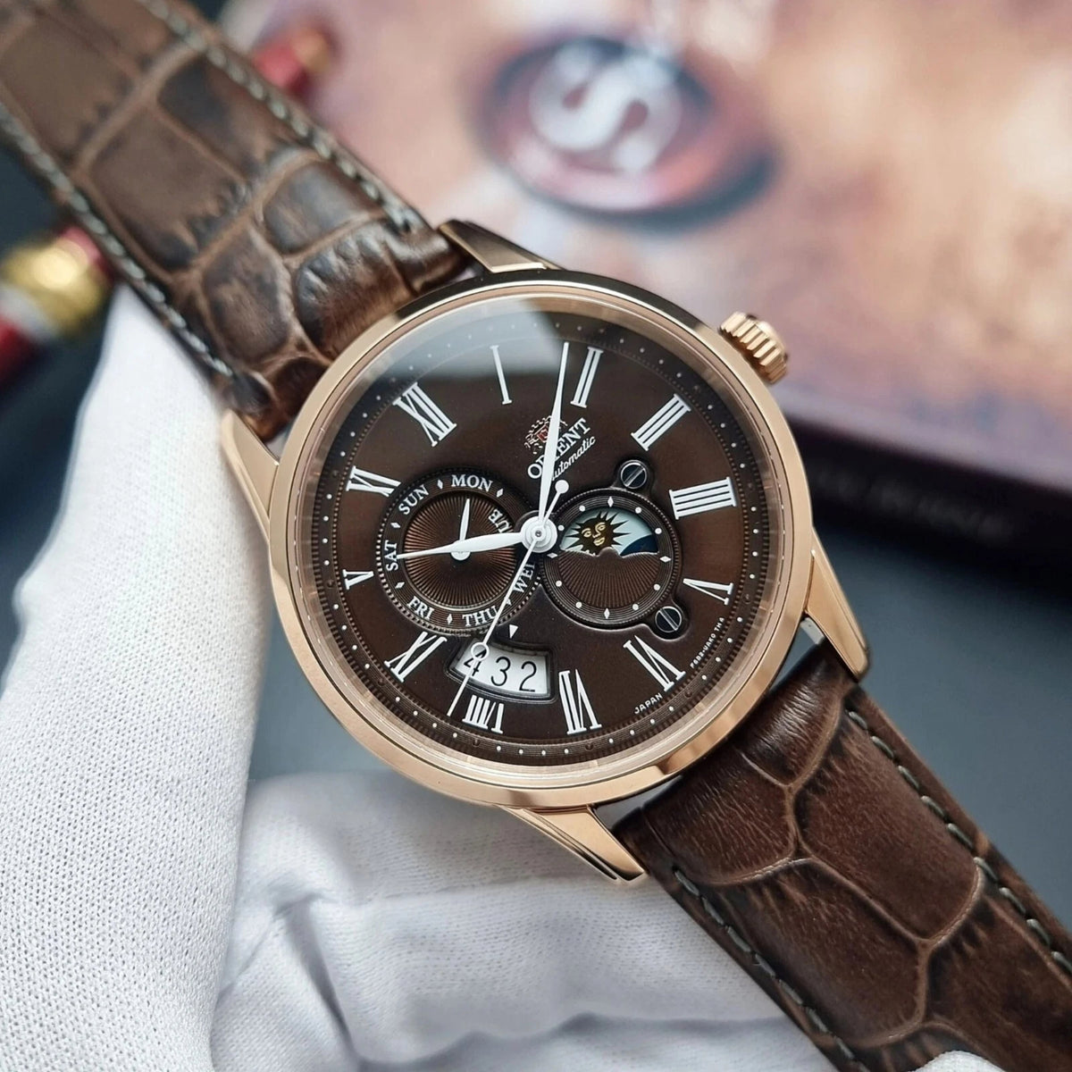 Orient Bambino Sun and Moon RA-AK0009T30B automatic wristwatch on wrist: brown leather strap, rose-gold case, dark dial with subdials