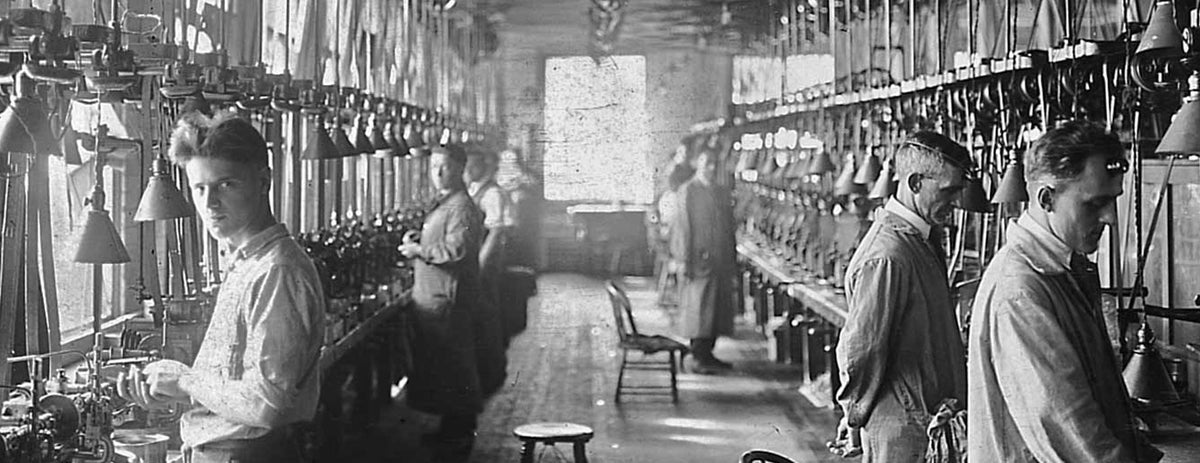 Black and white historical photo of watchmakers crafting timepieces on a factory assembly line