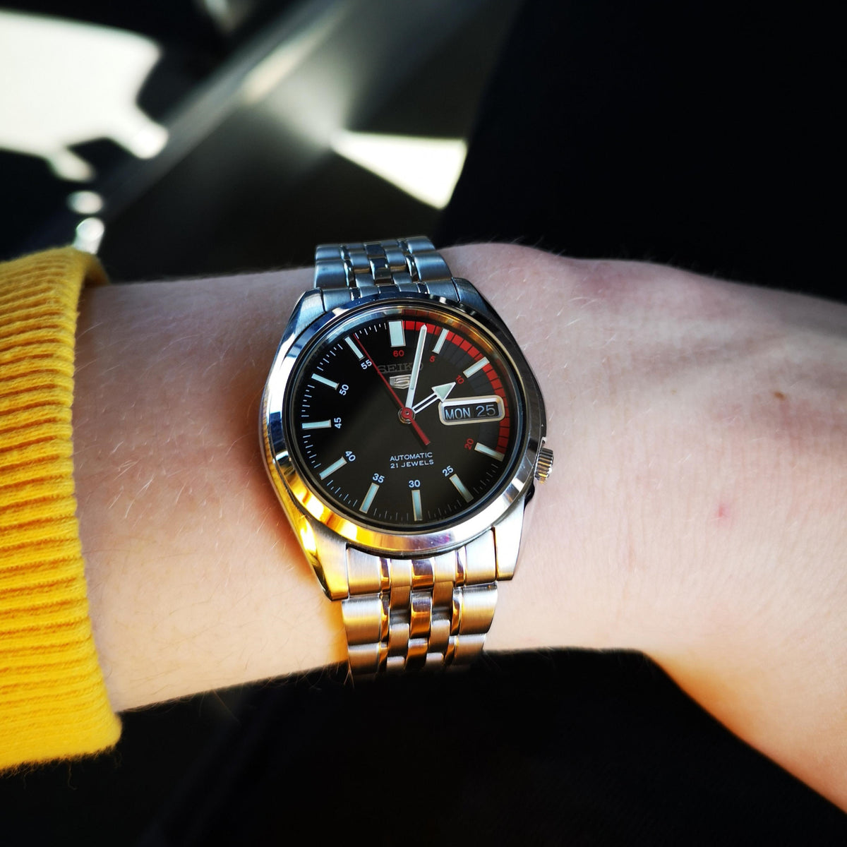 Seiko 5 SNK375K1 mens automatic wristwatch on wrist with black dial, red details, and day/date window