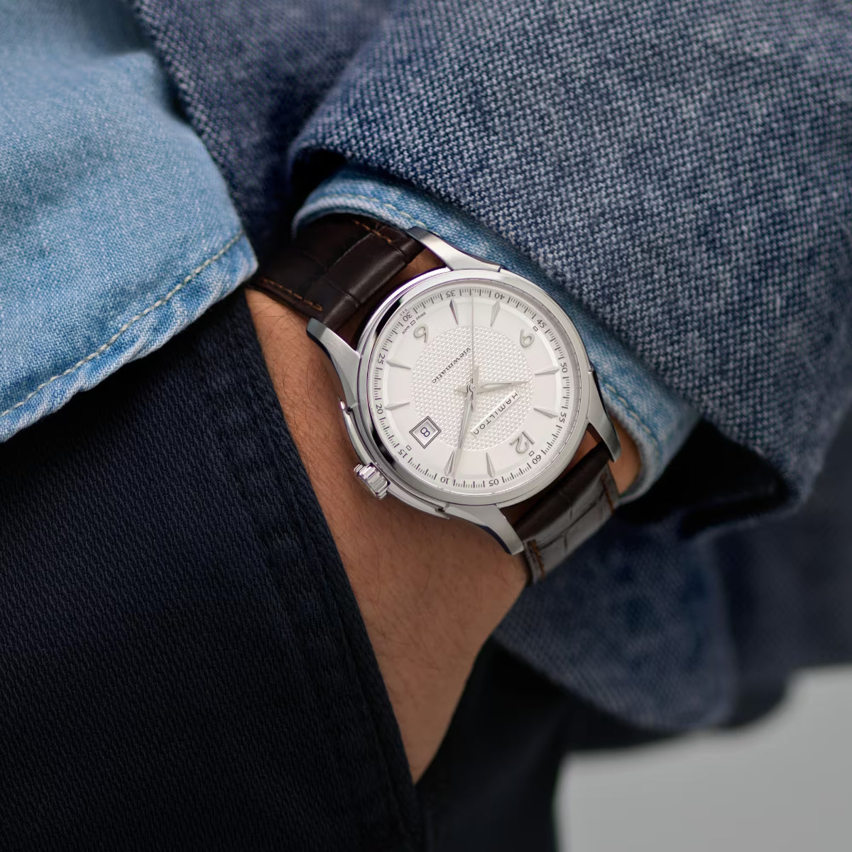 Men's wristwatch with brown leather strap and white dial under blue denim shirt