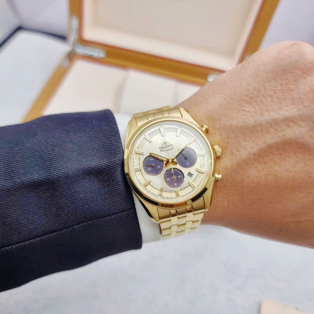 Gold solar chronograph watch with champagne dial and blue subdials on steel bracelet.